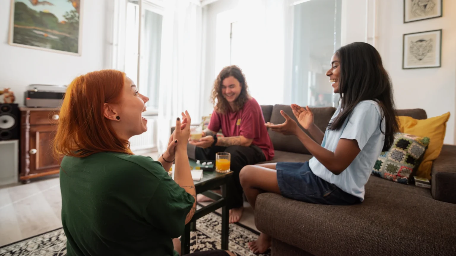 Kolme henkilöä nauravat yhdessä olohuoneessa.